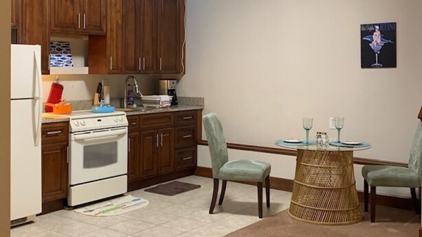 A kitchen with wooden cabinets, a white stove, and a dining area with two chairs and a small table. - Beach Side HideAway - Pet Friendly, WiFi, Smart TV, Central Heat/AC, Parking (Norfolk)