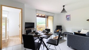A modern living room with a dining area, a TV, and a balcony with a view of the outdoors. - Apartment in Genos Near Lake Loudenvielle (Genos)