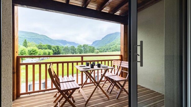 A wooden deck with a table and chairs, overlooking a scenic valley with mountains and a river. - Apartment in Genos Near Lake Loudenvielle (Genos)