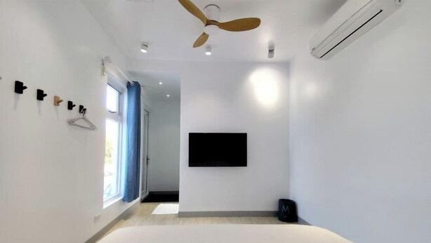 Una habitación de hotel moderna con cama, ventilador de techo, equipo de aire acondicionado, televisor montado en la pared y ventana con cortinas.