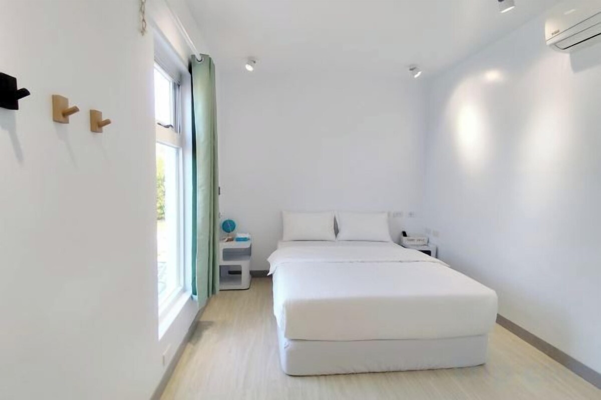 A modern bedroom with a large bed, a bedside table, a nightstand, and a window with curtains.