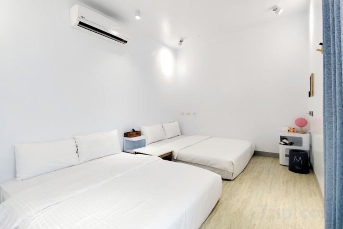 Une chambre d’hôtel avec deux lits, une petite table de chevet, une poubelle et un appareil de climatisation.