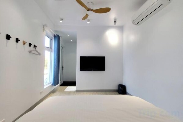 Una habitación de hotel moderna con una cama, ventilador de techo, televisor montado y una ventana con cortinas.