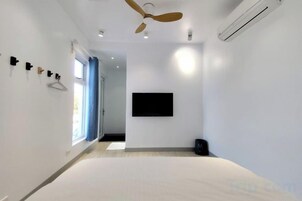 Una habitación de hotel moderna con una cama, ventilador de techo, televisor montado y una ventana con cortinas.