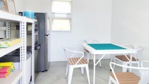 Una habitación pequeña con una mesa y sillas blancas, un refrigerador y una ventana.