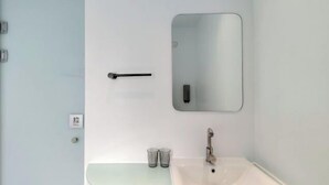 Un baño con un lavamanos blanco, un espejo y un perchero para toallas.