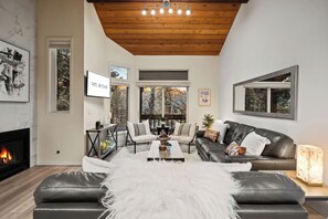 Una sala de estar moderna con chimenea, sofás de cuero, una mesa de centro y un ventanal con vistas a árboles.