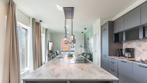 Une cuisine moderne avec un îlot en marbre, des meubles gris et des luminaires suspendus.