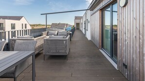 Une terrasse en bois avec des meubles d’extérieur, une porte vitrée et une vue sur les environs.
