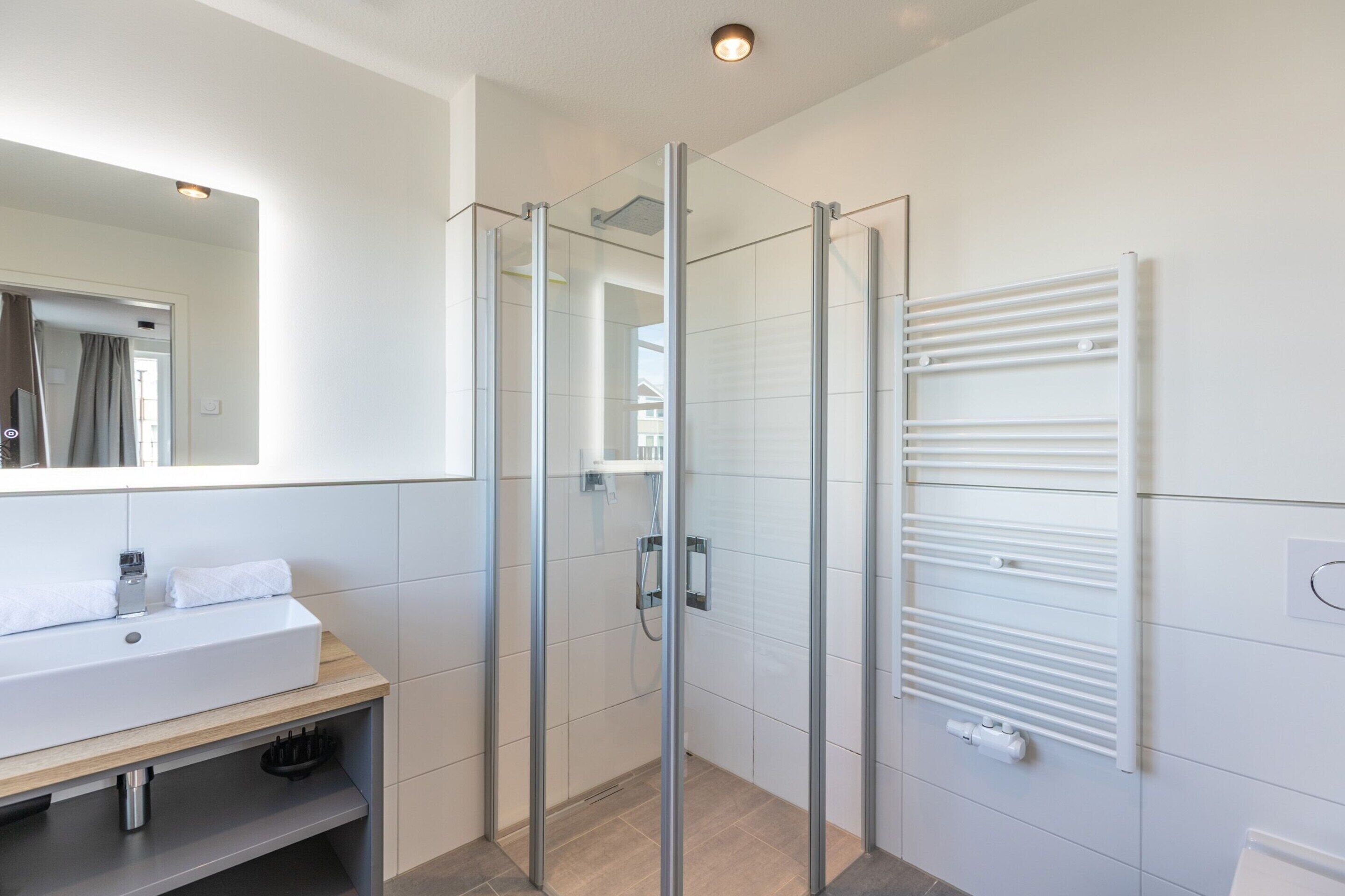 A modern bathroom with a glass shower enclosure, a white sink, and a built-in towel rack.