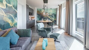 Un salon moderne avec un canapé, un pouf et une table basse agrémentée de vases. On y trouve également un coin repas avec une table et des chaises, et une cuisine en arrière-plan.