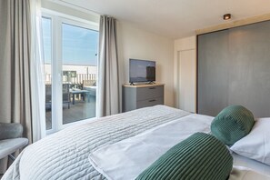 A hotel room with a bed, a TV on a wooden stand, a sliding door to a balcony, and a chair. - Luxusapartement mit Meerblick (Nordstrand)