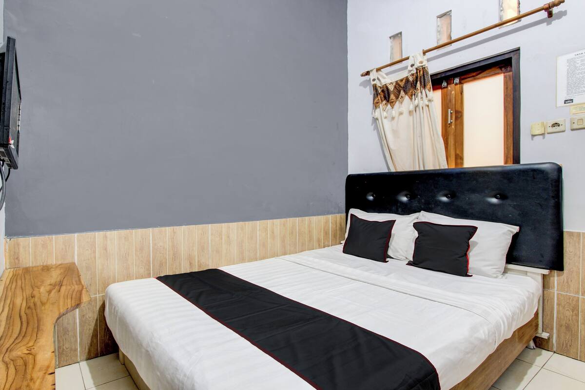 Una cama bien hecha con una colcha a rayas negras y blancas, un cabecero de madera y una mesita de noche al lado.
