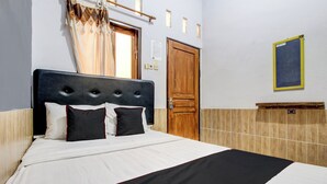 Ein ordentlich bezogenes Bett mit grau-weiß gestreifter Tagesdecke, einem Holz-Kopfteil und zwei schwarzen Kopfkissen.