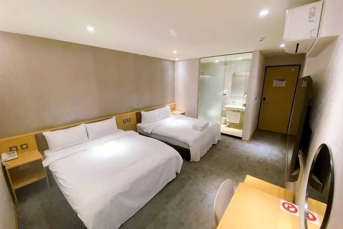 Une chambre d’hôtel avec deux lits, un bureau, une chaise, un miroir et une porte donnant sur une salle de bain.