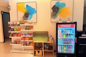 A vending machine with snacks and Coca-Cola, a shelf with various items, and abstract art on the wall. - MICHI HOTEL (Taoyuan)