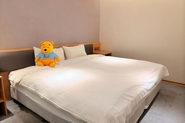 A neatly made bed with a plush toy and pillows, a wooden headboard, and a nightstand with a lamp. - MICHI HOTEL (Taoyuan)