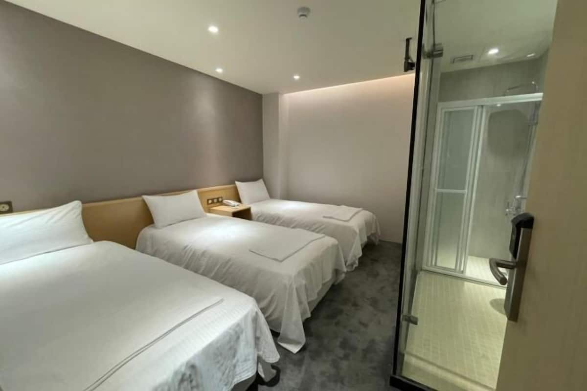 A hotel room with two beds, a shower, and a glass door.