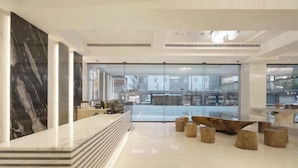 A modern lobby with a marble reception desk, glass doors leading to a dining area, and wooden stools. - Gamalan Star Hotel (Yilan)