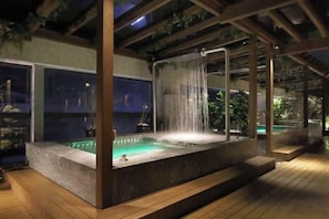 A hot tub with a waterfall feature, surrounded by wooden decking and under a pergola structure. - Gamalan Star Hotel (Yilan)