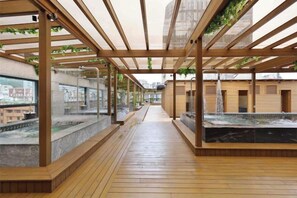A covered outdoor area with wooden flooring, glass walls, and a water feature. - Gamalan Star Hotel (Yilan)