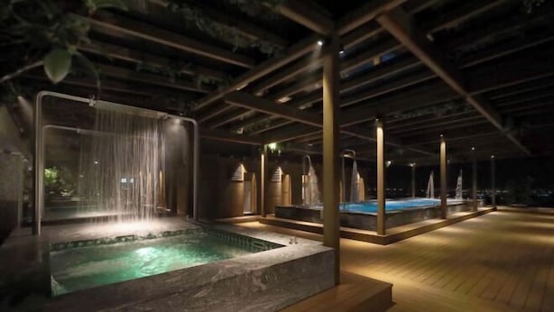 A nighttime outdoor hot tub area with a waterfall feature, wooden deck, and a pool. - Gamalan Star Hotel (Yilan)