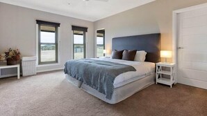 A bedroom with a large bed, two windows, a ceiling fan, and a white door. - Iris Acres Modern Farmhouse Portland (Lithgow)