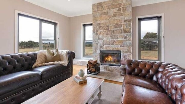 A living room with a stone fireplace, leather sofas, and large windows. - Iris Acres Modern Farmhouse Portland (Lithgow)
