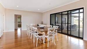 A spacious dining area with a round table and white chairs, large sliding glass doors leading to an outdoor patio. - Iris Acres Modern Farmhouse Portland (Lithgow)
