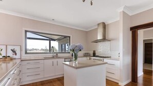 A modern kitchen with white cabinetry, a central island, and a large window. - Iris Acres Modern Farmhouse Portland (Lithgow)