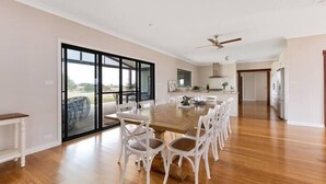A spacious dining area with a large wooden table and white chairs, a ceiling fan, and a sliding glass door leading to a balcony. - Iris Acres Modern Farmhouse Portland (Lithgow)