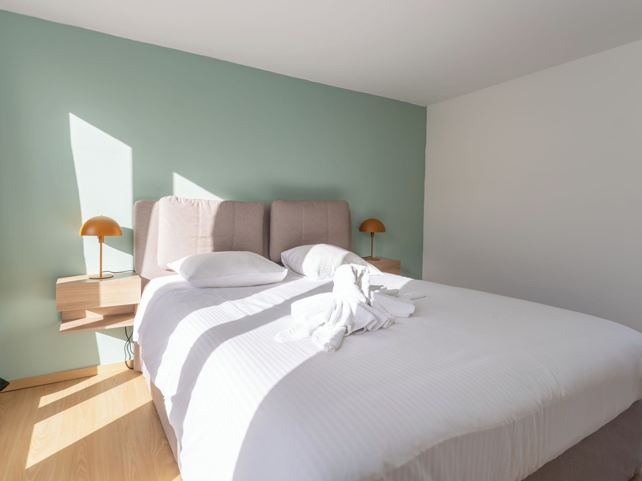 A neatly made bed with white linens and two bedside lamps.