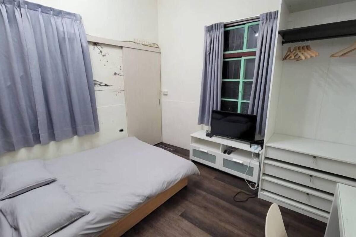 Una camera da letto piccola e ordinata con un letto singolo, una TV su un mobile e un armadio con spazio per appendere i vestiti.