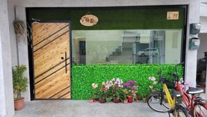 Une devanture de magasin avec une porte en bois, une haie verte et des plantes en pot.