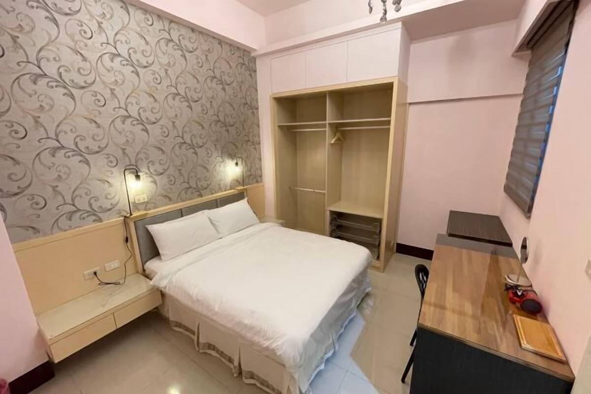 A bedroom with a bed, bedside table, wardrobe, and a desk with a chair.