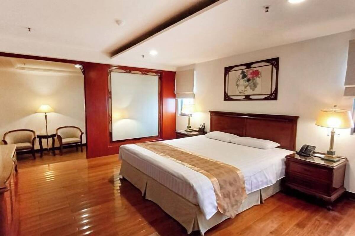 A hotel room with a large bed, bedside tables, a chair, a desk, and a large window.