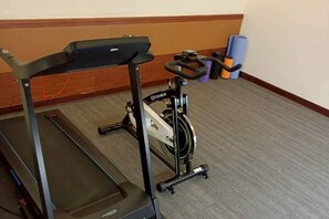 A stationary bike and treadmill in a room with carpeted flooring and a wooden baseboard. - Hi-YES HOTEL TAOYUAN (Taoyuan)