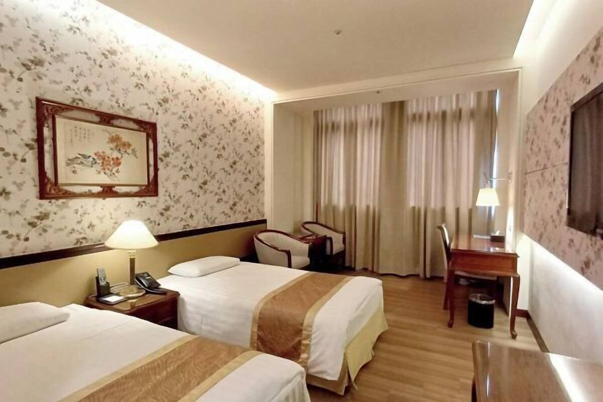 A hotel room with two beds, a desk, a chair, a lamp, a telephone, and a framed picture on the wall.