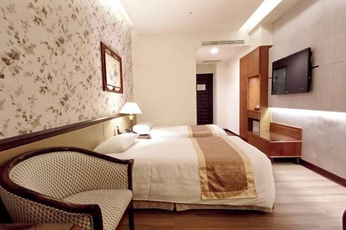 A hotel room with a bed, a chair, a TV mounted on the wall, and a door leading to another room.
