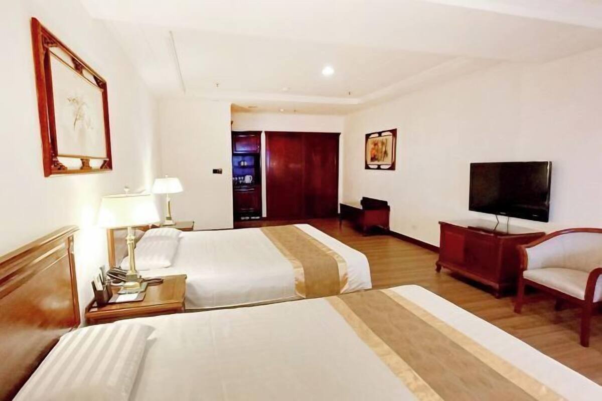 A hotel room with two beds, a TV, a desk with a lamp, and a chair.