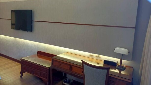 A room with a desk, a chair, a television mounted on the wall, and a small table with a lamp. - Hi-YES HOTEL TAOYUAN (Taoyuan)