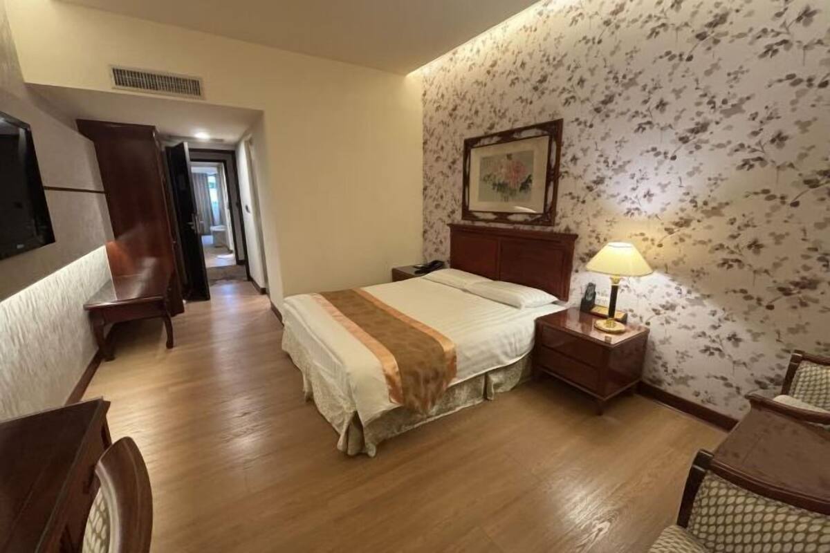 A hotel room with a bed, bedside table, lamp, and a painting on the wall.