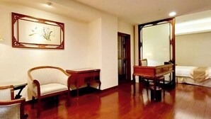 Une chambre d’hôtel avec un plancher en bois, un lit recouvert d’une courtepointe blanche, une chaise en bois, une petite table en bois et un tableau encadré accroché au mur.