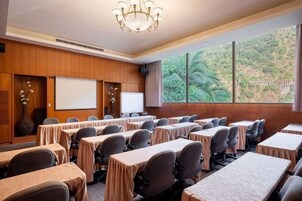 A conference room with tables, chairs, a projector screen, and a large window with a view of greenery.