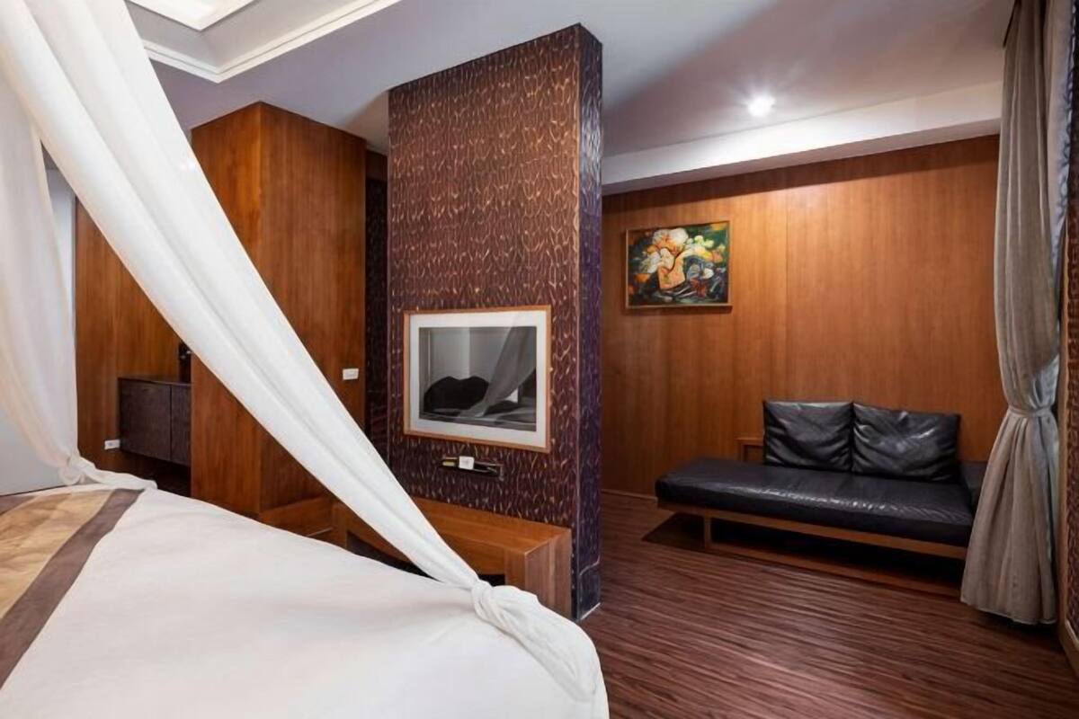 A bedroom with a bed, a TV, a sofa, and a wall-mounted TV.