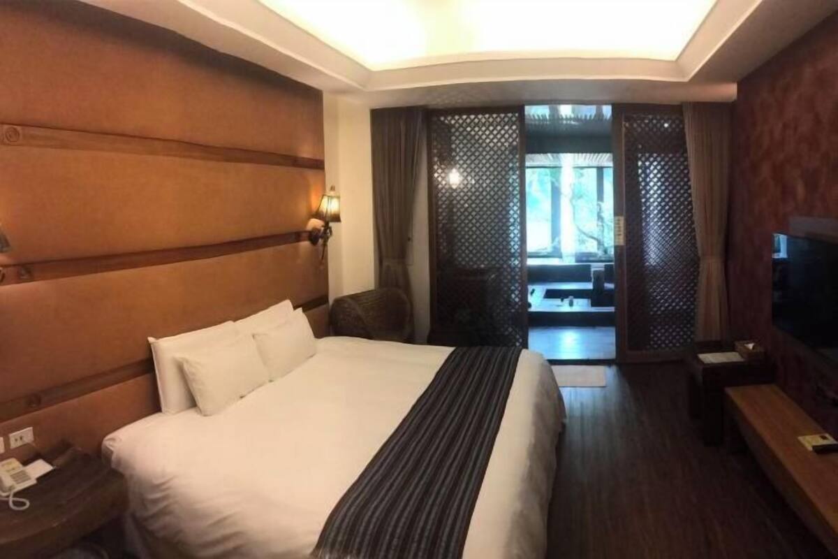 A hotel room with a large bed, a TV, a desk, and a view of a balcony.