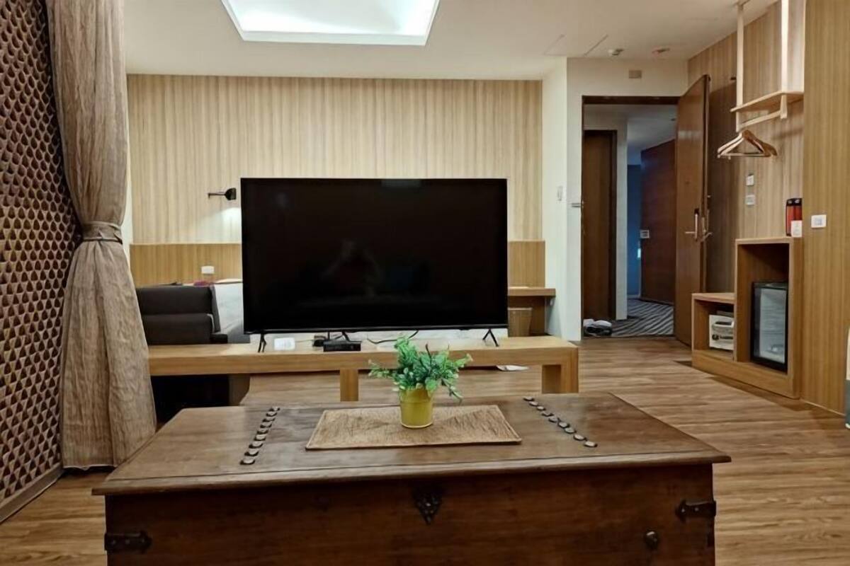 A modern living room with a large flat-screen TV, wooden furniture, and a potted plant.