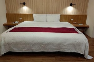 A large bed with white linens and a red throw blanket, two bedside tables with lamps, and a wooden headboard.