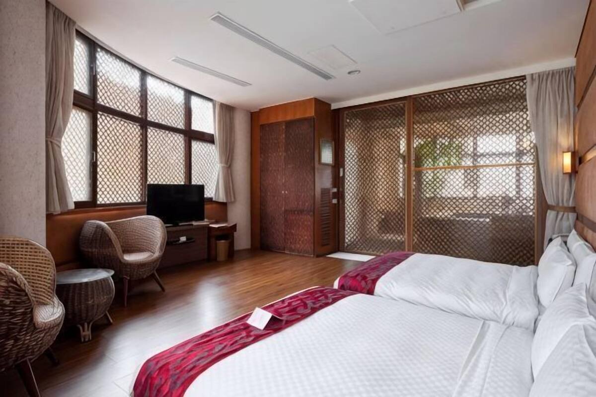 A hotel room with a bed, a television, a seating area with chairs, and a large window.