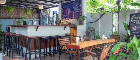 Un restaurant avec des tables et des chaises en bois, un coin bar et un tableau affichant le menu.